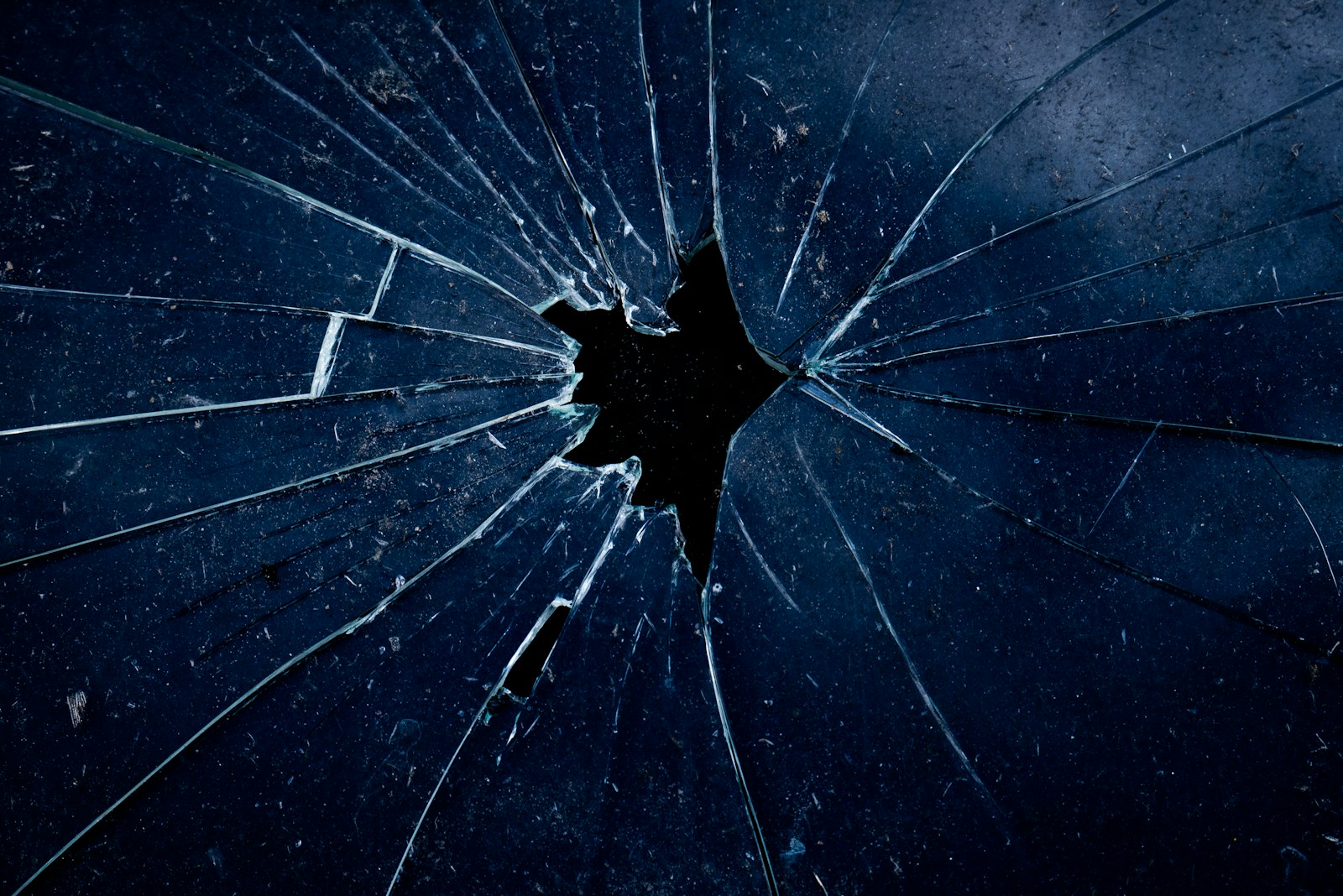 A dark blue glass surface with a central hole and radiating cracks