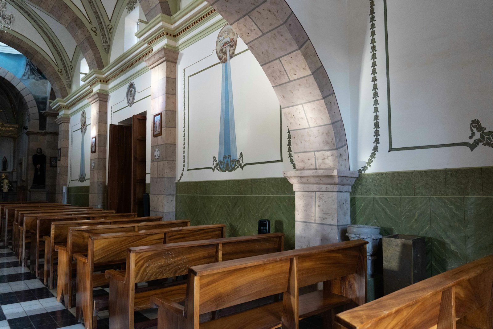 Wooden pews in a church with stone arches and painted wall murals