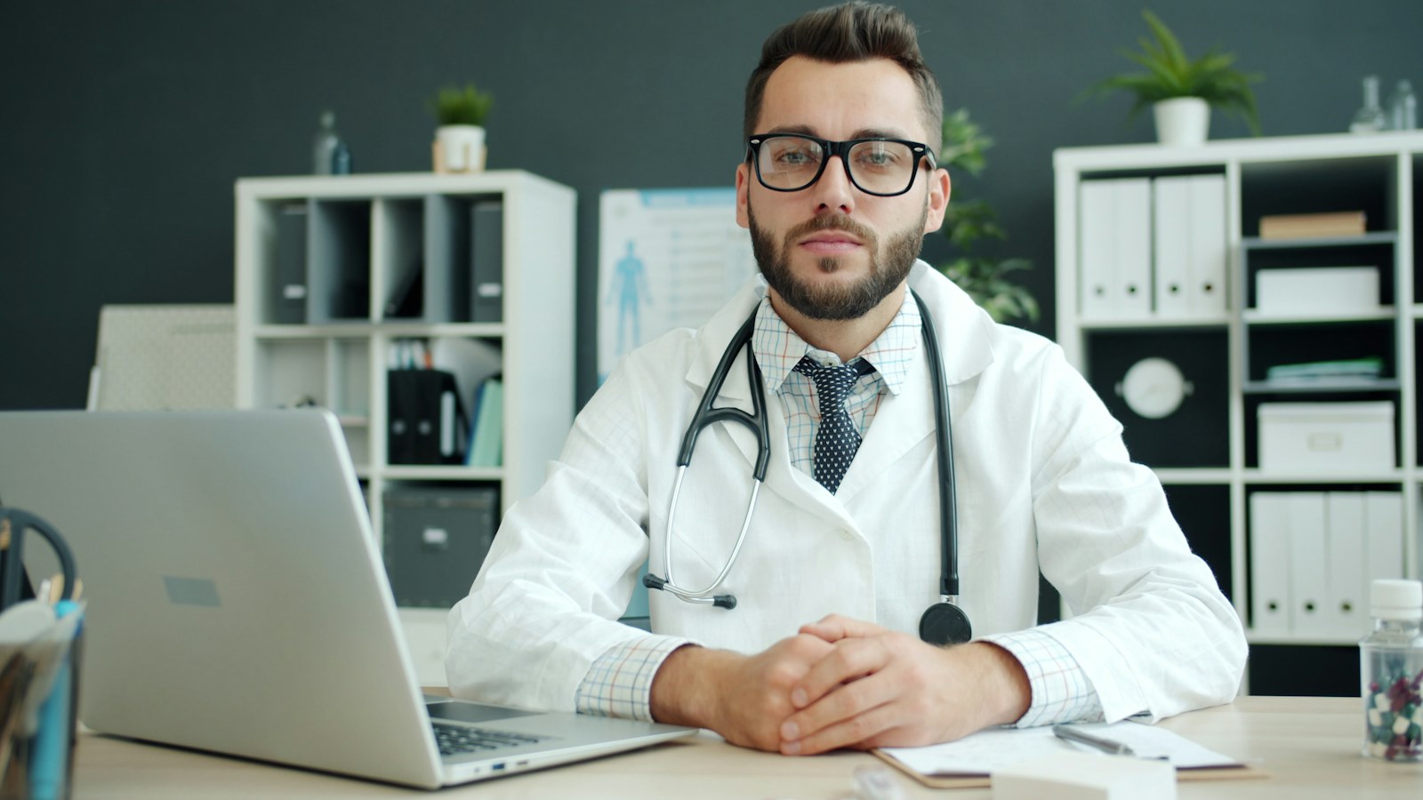 Doctor wearing a white coat sits at a desk