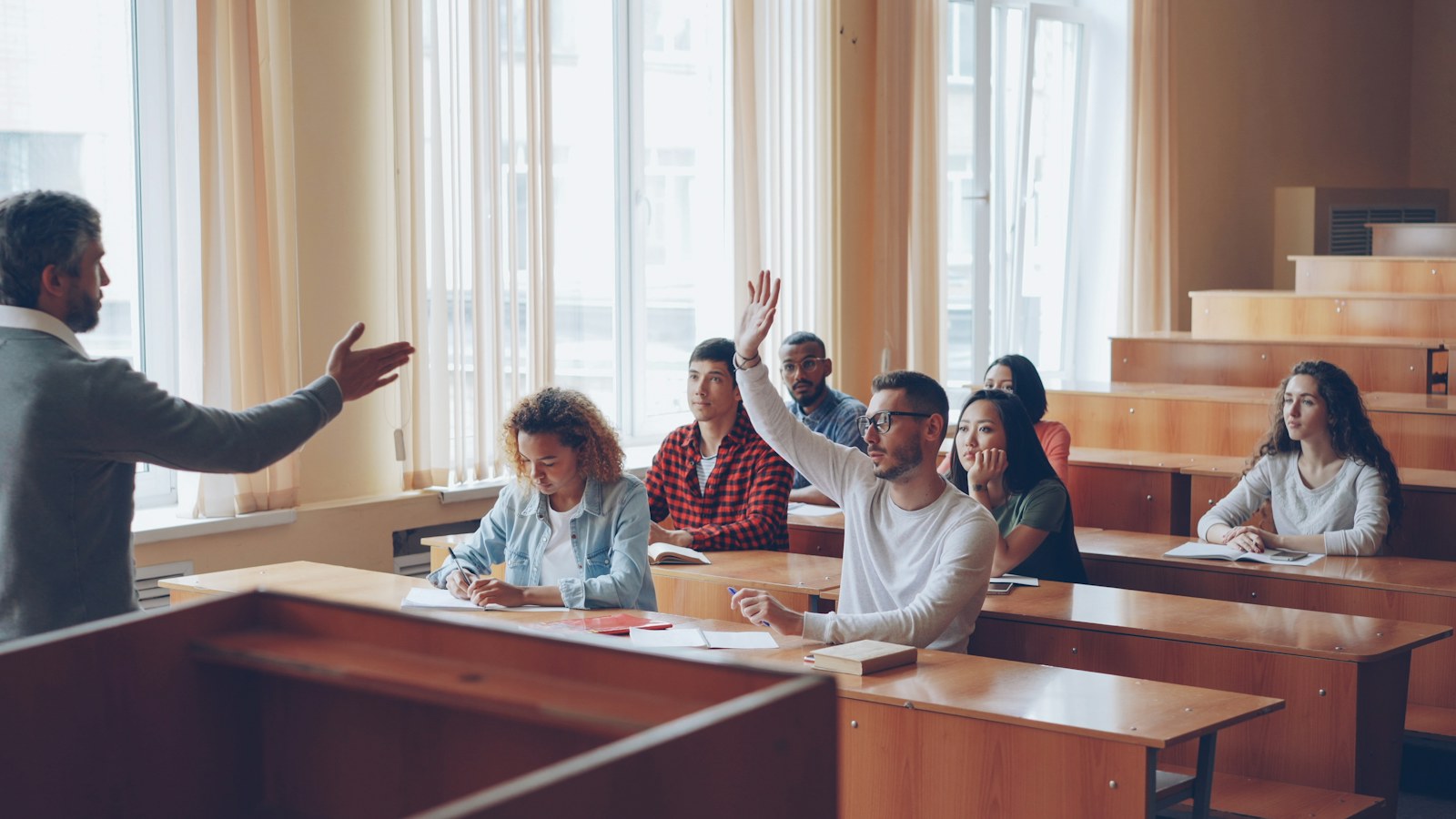Students raising hands in a lecture hall classroom