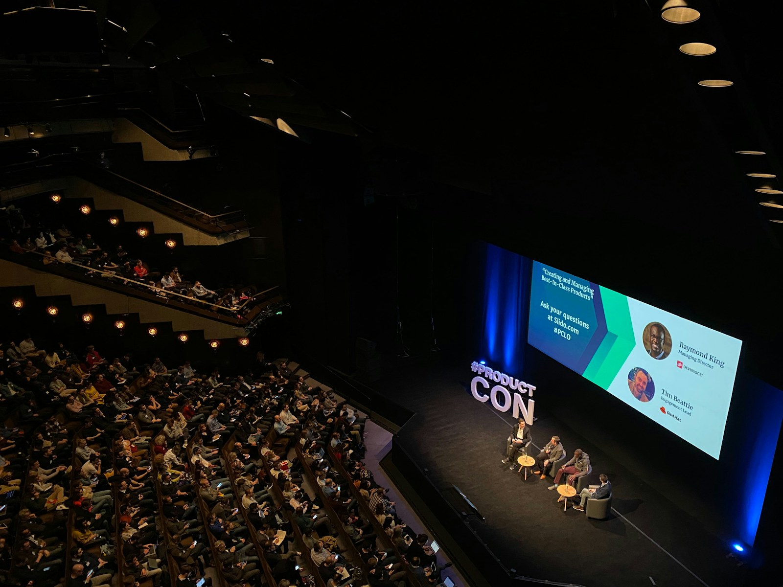 A panel discussion on a stage in a large auditorium with an audience