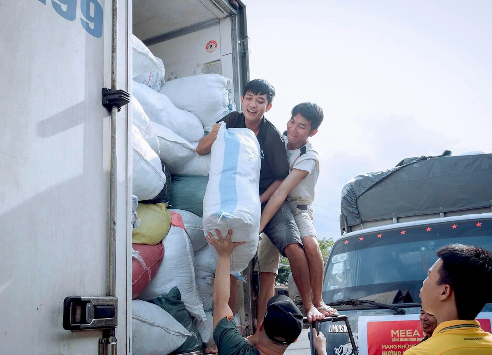 Three men loading large white sacks into the back of a delivery truck