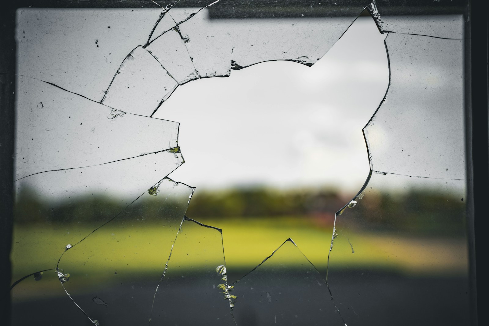 a broken glass window with a field in the background