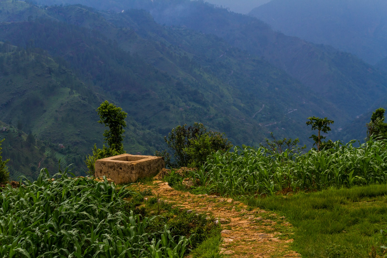 Stone well on a grassy hillside with mountains behind
