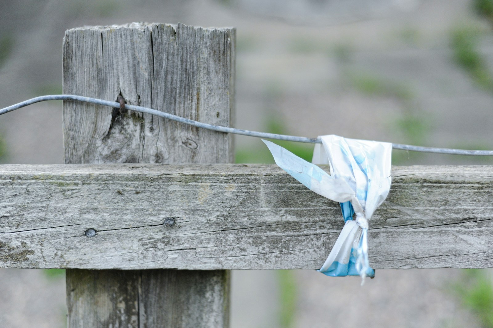 A weathered wooden fence post with a wire and a tied plastic strip