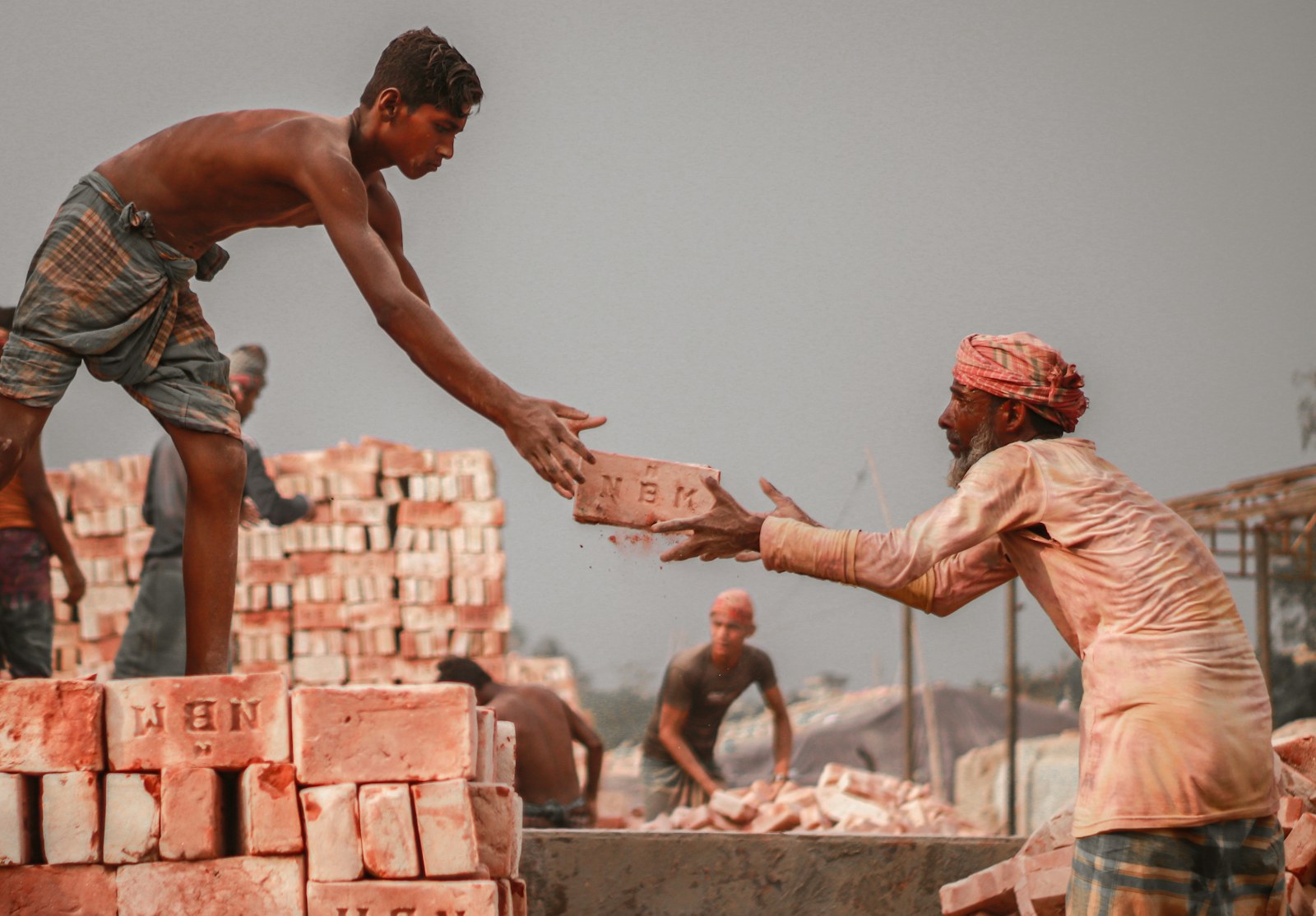 A man passing a brick to another man at a brickyard