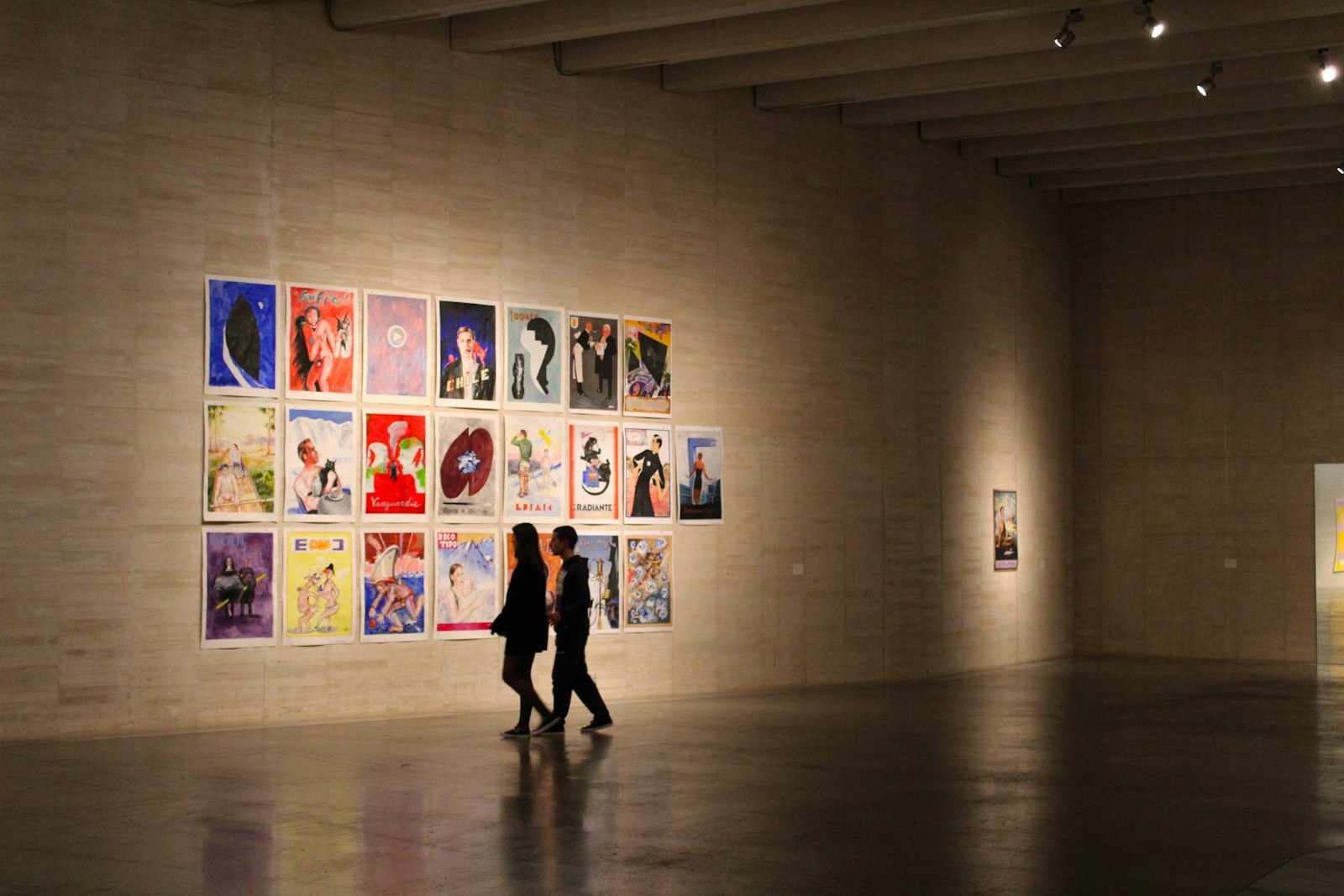 a man and woman standing in a room with a wall of paintings