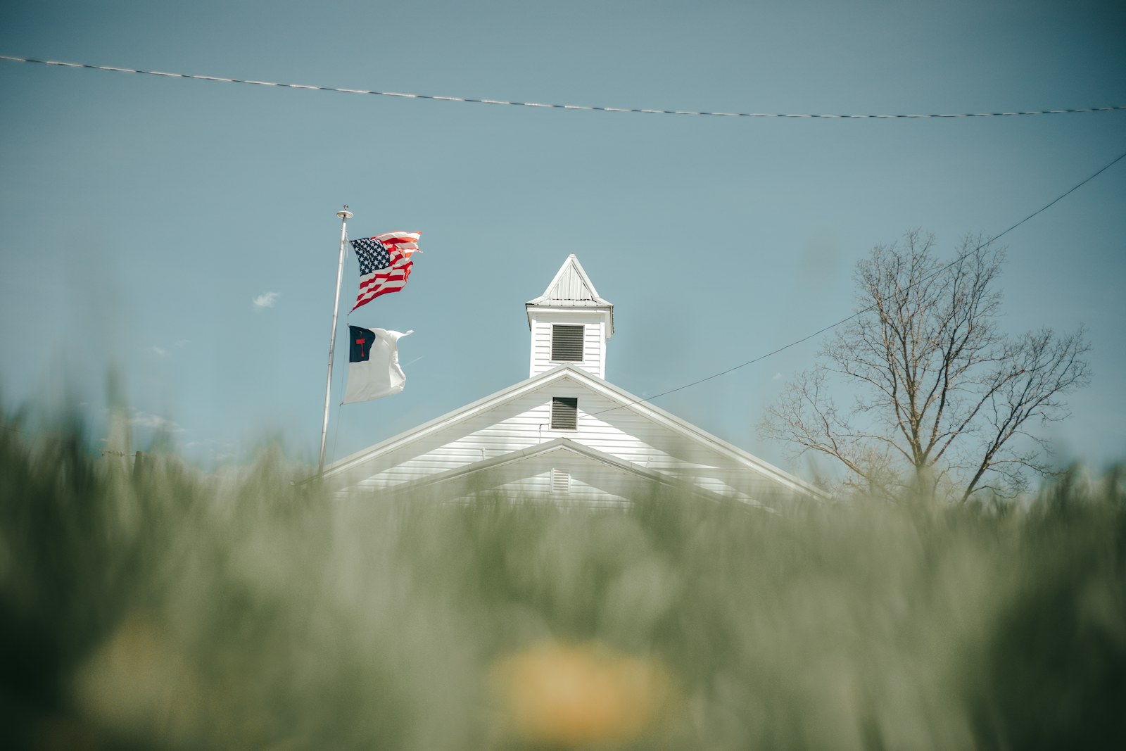 A white church with flags, seen through the grass