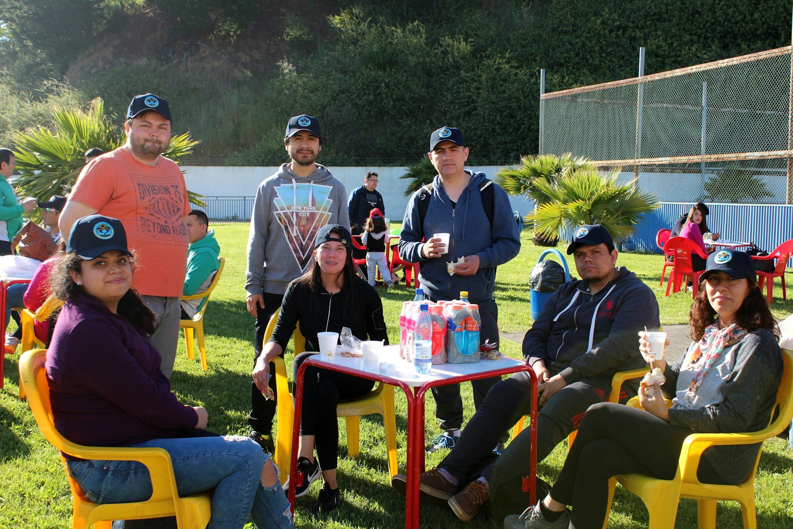 A group of adults wearing matching caps at a table on a sunny lawn