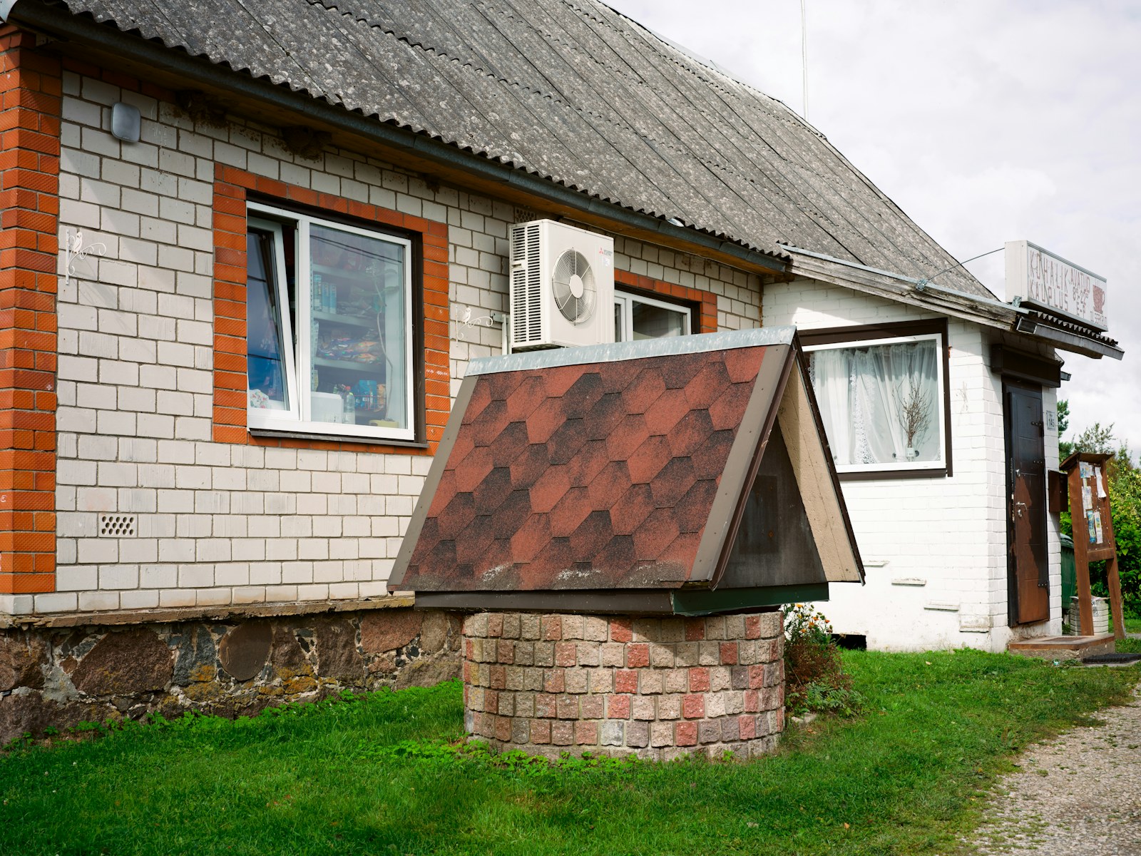 A stone well with a red shingled roof in front of a brick building