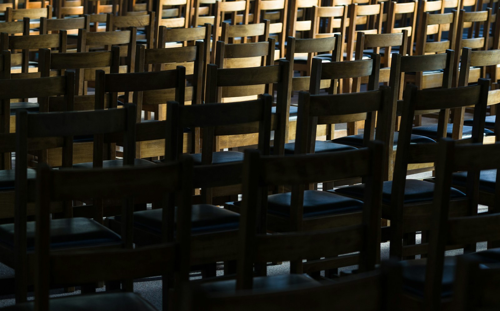 Rows of empty wooden chairs in dim light