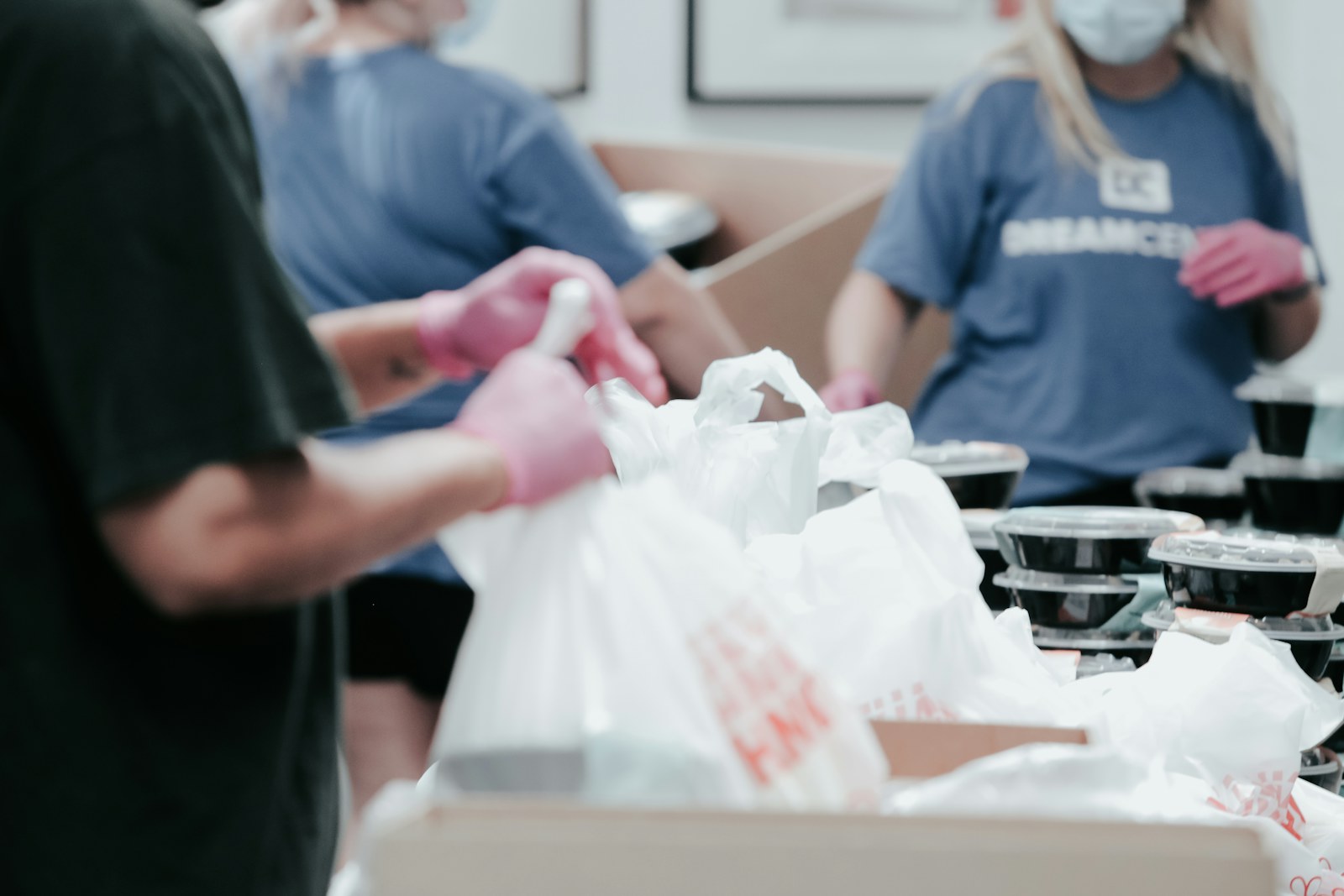 People in blue shirts and pink gloves packing food into white plastic bags