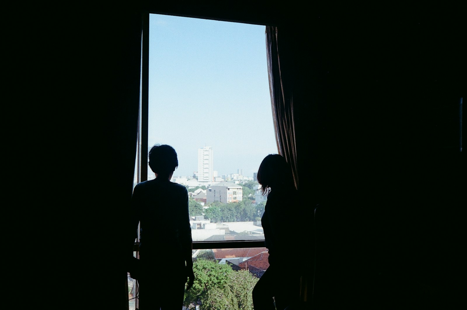 Two silhouetted figures look out of a window