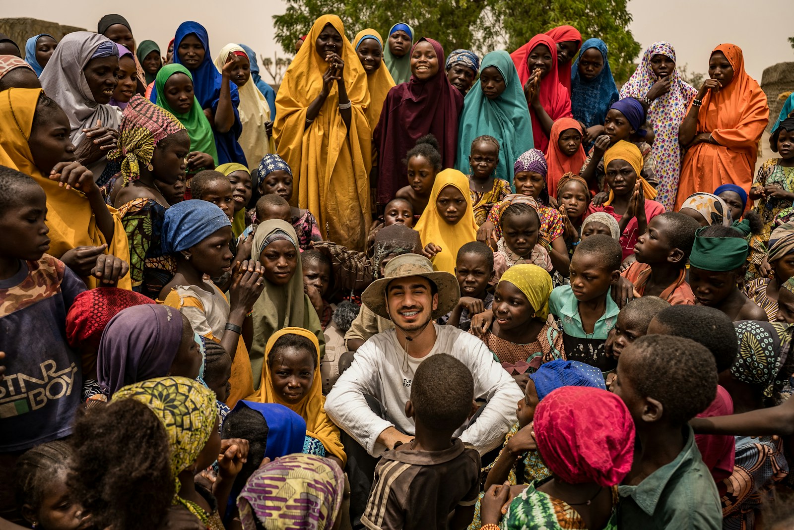A man smiles surrounded by many happy children and women