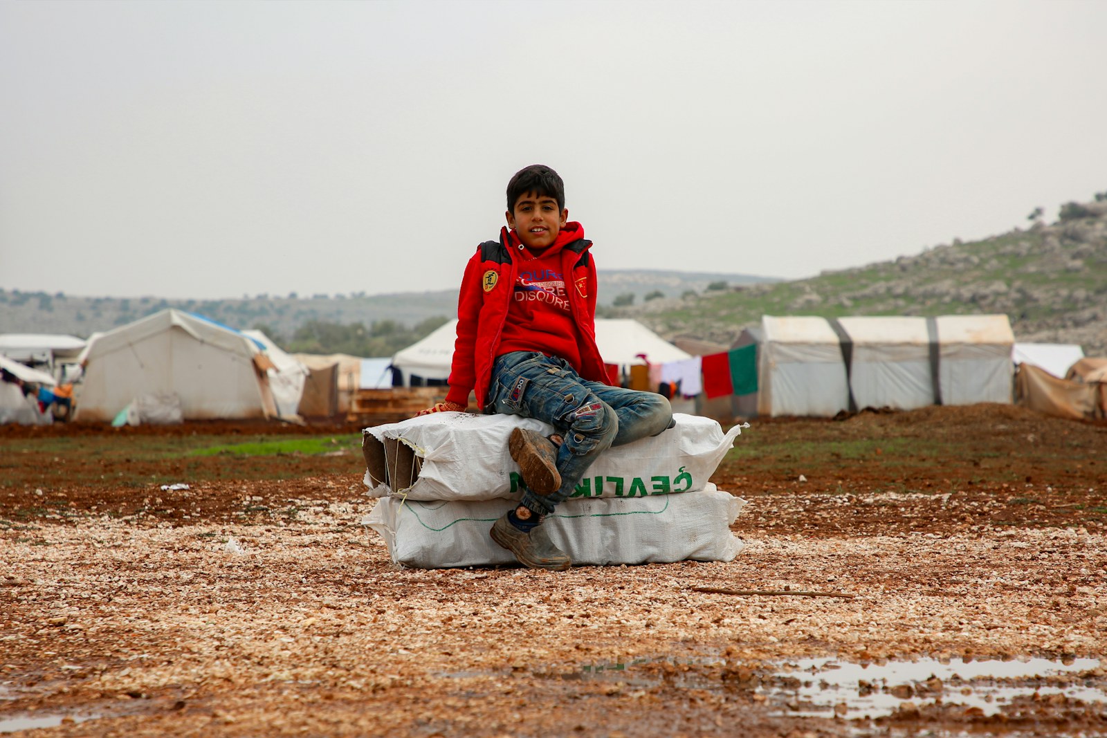 A young boy sitting on top of a bag in the mud