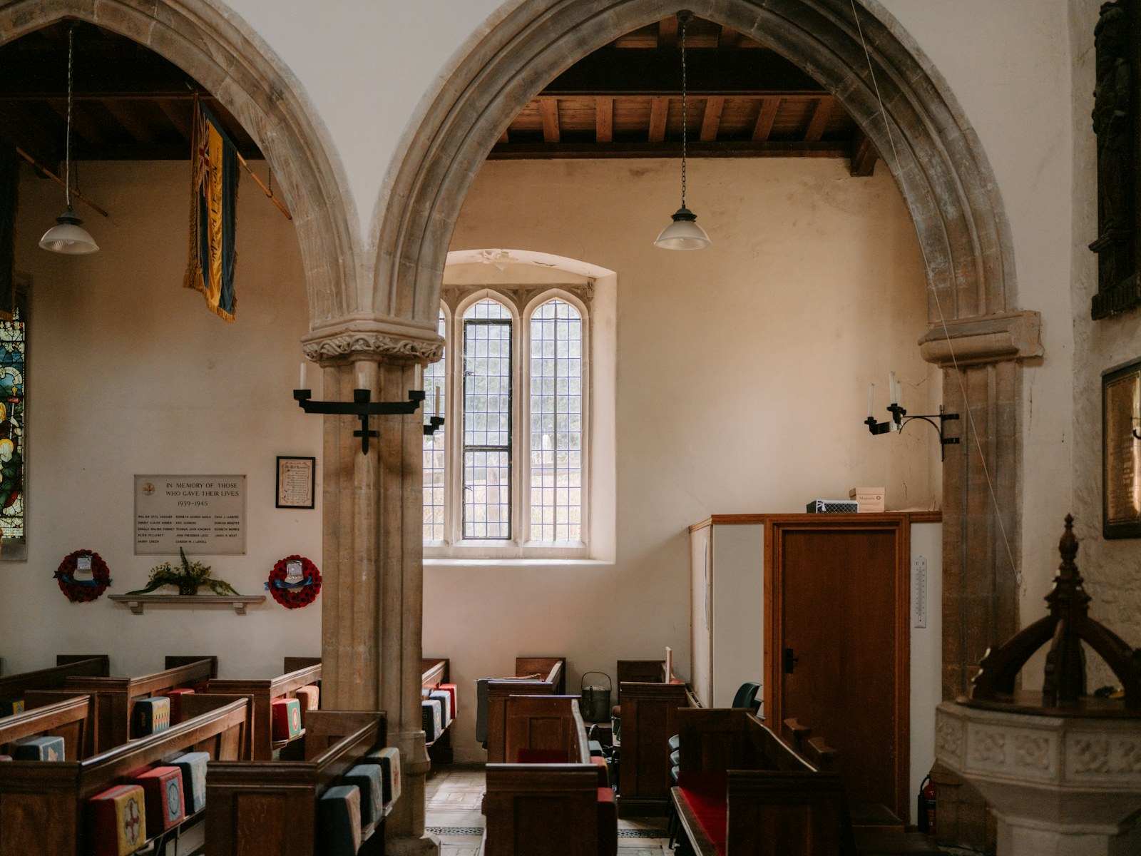Wooden pews inside a stone church with arched doorways and a memorial plaque