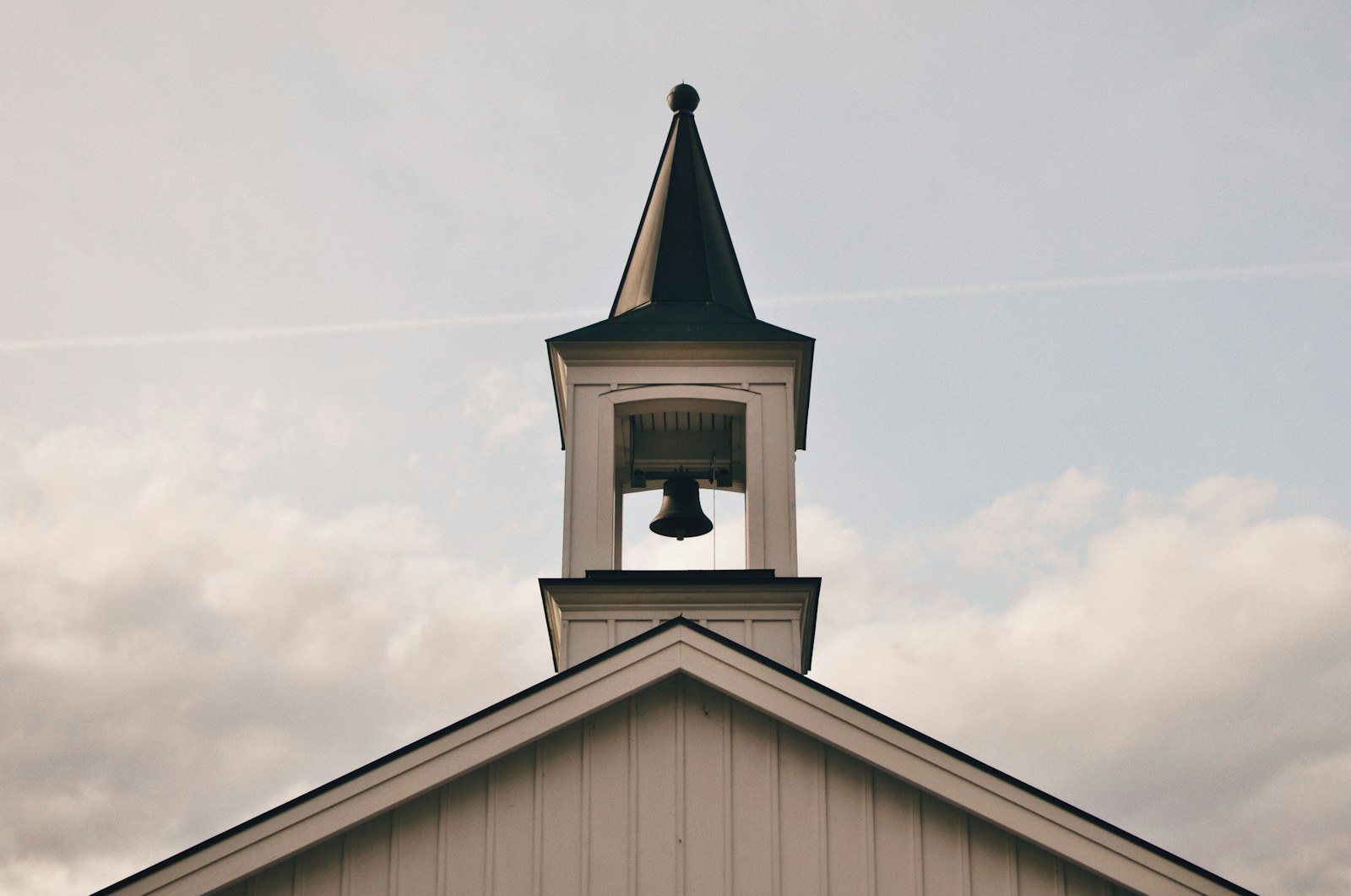 A white wooden bell tower with a dark spire against a cloudy sky