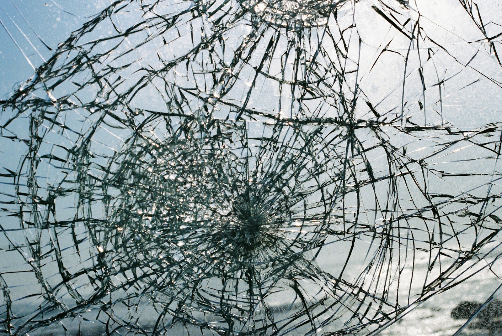 A broken windshield of a car with a blue sky in the background