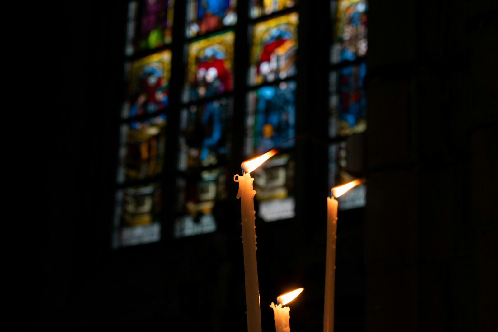 three candles in front of a stained glass window