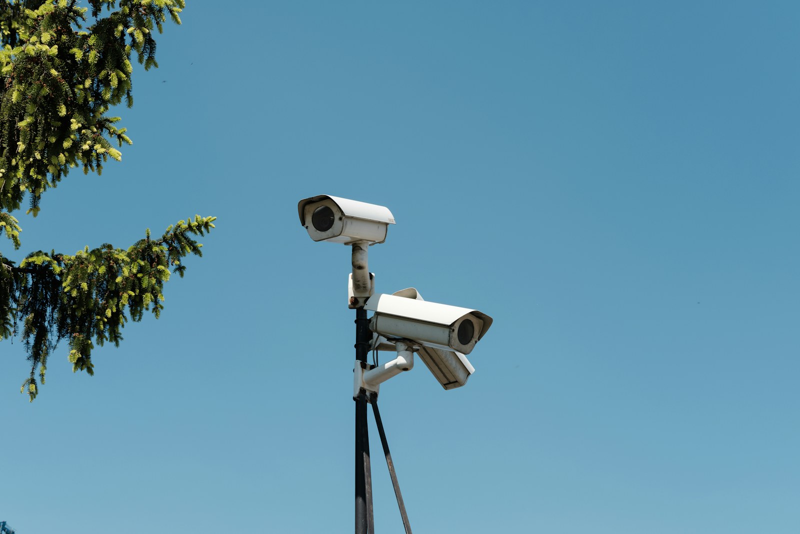 Two white security cameras mounted on a pole against a clear blue sky